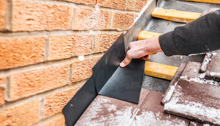 Lead flashing being dressed against a brick wall on a tiled roof